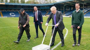 Prime Minister Boris Johnson paints over the white line of the centre circle during a visit to Bury FC at their Gigg Lane ground in Bury, Greater Manchester