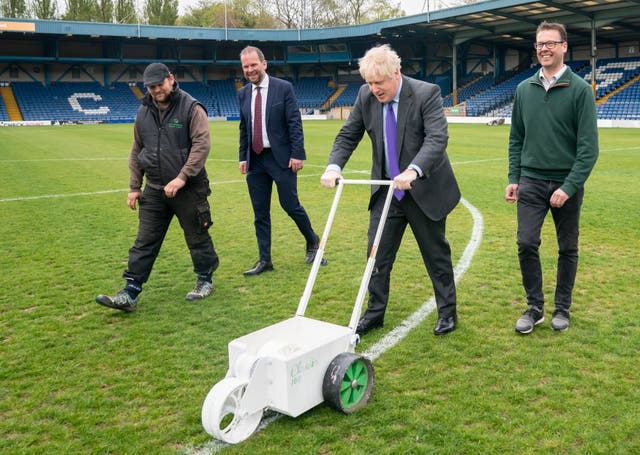 Prime Minister Boris Johnson paints over the white line of the centre circle during a visit to Bury FC at their Gigg Lane ground in Bury, Groter Manchester