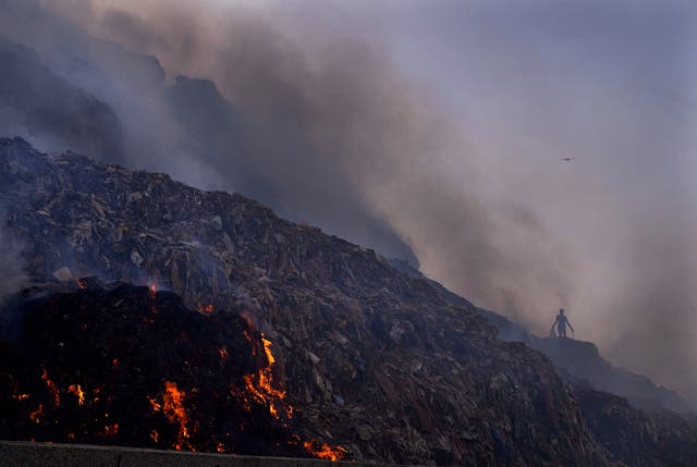 A ragpicker looks for reusable items while a fire rages at the Bhalswa landfill in New Delhi