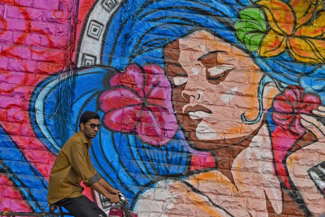A man rides his bicycle past a wall mural in Mumbai