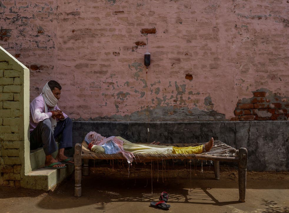 <p>A man sits next to his wife, who was suffering from a high fever, as she intravenously receives rehydration fluid at a makeshift clinic in Parsaul village, Uttar Pradesh on 22 May 2021</磷>