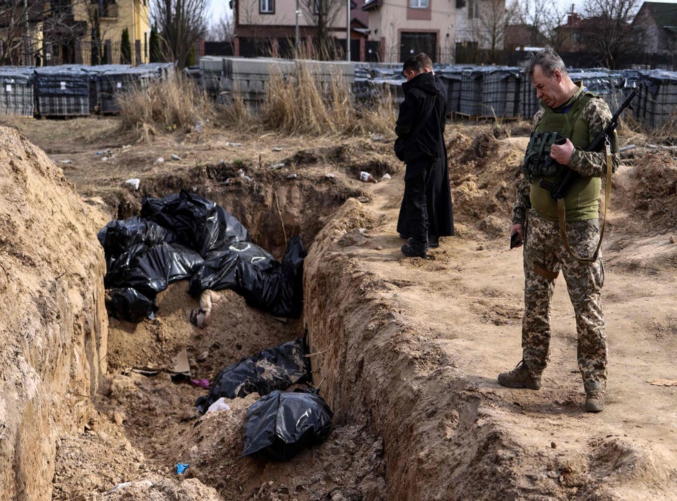 <p>A Ukranian soldier looks at body bags as priests pray at a mass grave in the grounds surrounding St Andrew’s Church in Bucha</p>