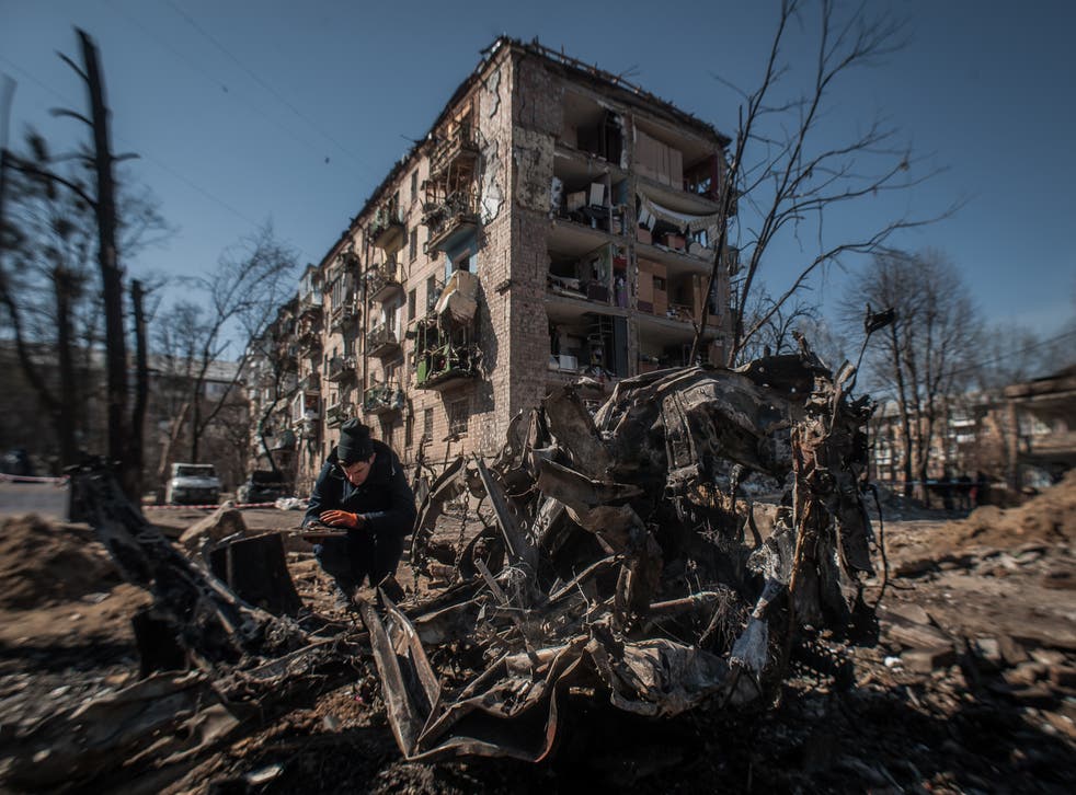 <p>A man disassembles parts of a burned car near the destroyed houses in Kyiv</磷>
