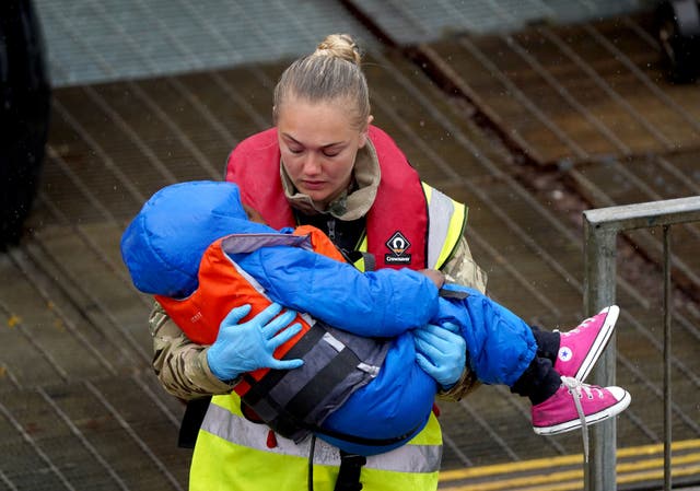 A young child amongst group of people thought to be migrants is carried by a member of the military as they are brought in to Dover, Kent