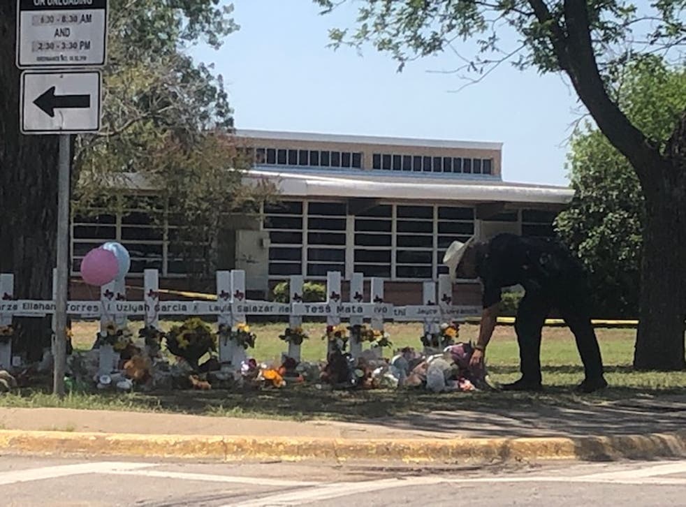 <p>A law enforcement officer lays flowers brought by locals - who were not allowed beyond a certain point as officials prepared for a Thursday press conference - at the memorial outside of Robb Elementary School in Uvalde</磷>