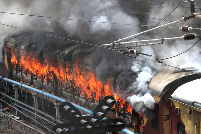 Flames rise from a train set on fire by protestors at Secundrabad railroad station in Hyderabad, Índia,
