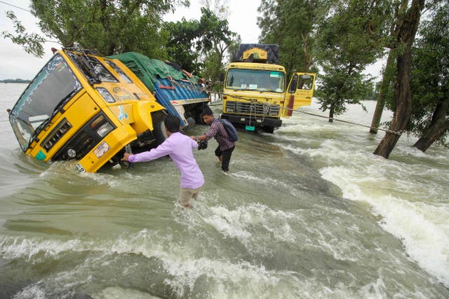 People wade past stranded trucks on a flooded street in Sunamganj