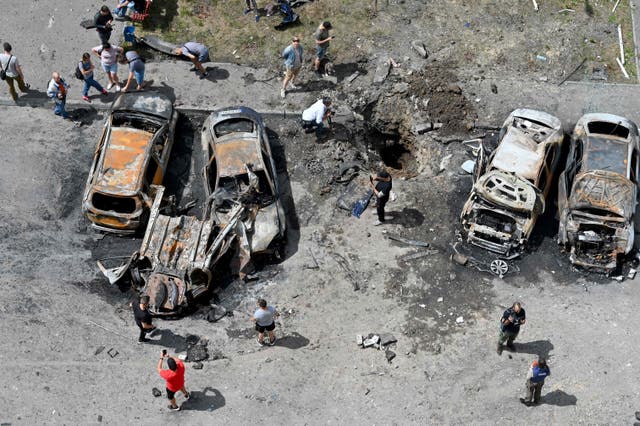 Bystanders gather around the wreckage of vehicles and a crater after Russian missiles struck the courtyard of a multi-storey residential complex on the eastern outskirts of Kharkiv, ウクライナ