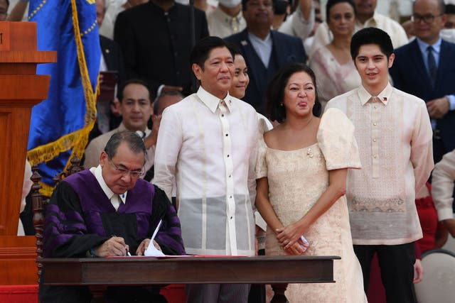 フィリピン新大統領フェルディナンド・マルコス・ジュニア. (C) と妻のルイーズは、アレクサンダー・ジェスムンド最高裁判所長官として見守っています (L) マニラの国立博物館での新大統領の宣誓式の後、就任宣誓書に署名する