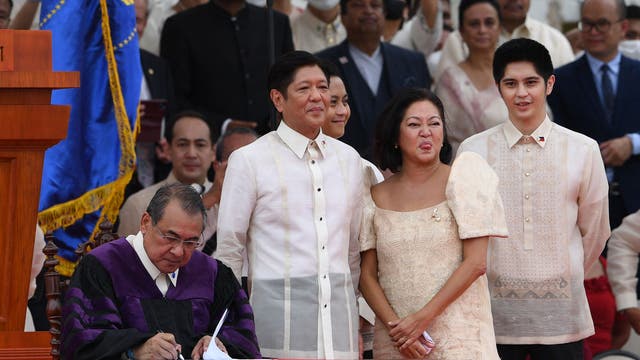 フィリピン新大統領フェルディナンド・マルコス・ジュニア. (C) と妻のルイーズは、アレクサンダー・ジェスムンド最高裁判所長官として見守っています (L) マニラの国立博物館での新大統領の宣誓式の後、就任宣誓書に署名する