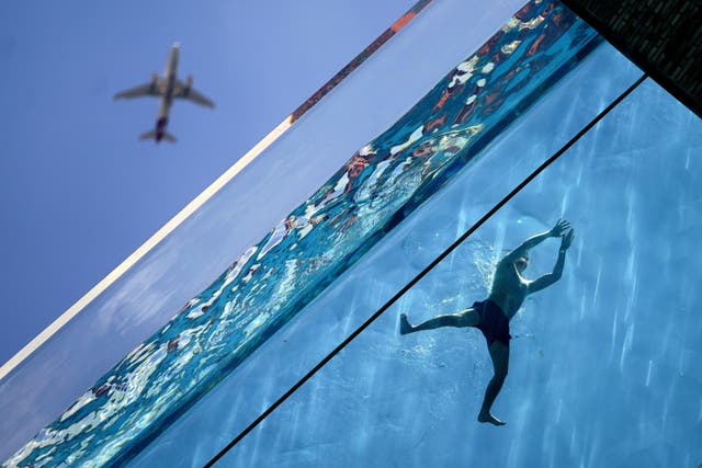 A man swims in the Sky Pool, a transparent swimming pool suspended 35 meters above ground between two apartment buildings, during hot weather in Nine Elms, central London