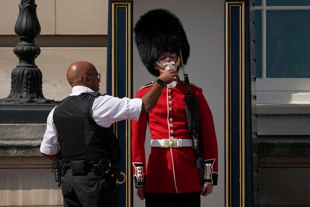 警察官が伝統的なクマの皮の帽子をかぶった兵士に水を与える, バッキンガム宮殿の外で警備中. 政府は史上初の猛暑に対する赤警報を発令