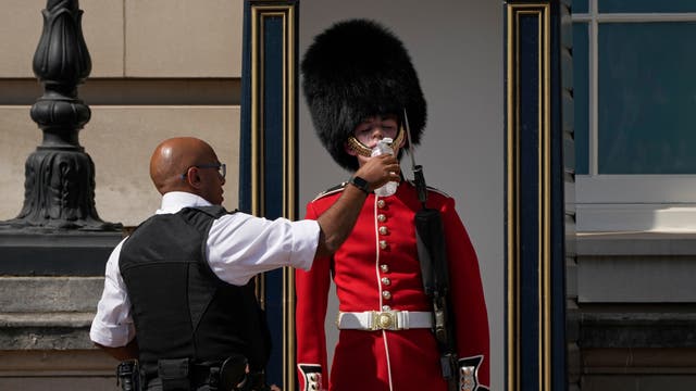 一名警察给戴着传统熊皮帽的士兵送水, 在白金汉宫外执勤. 政府首次发布极端高温红色预警