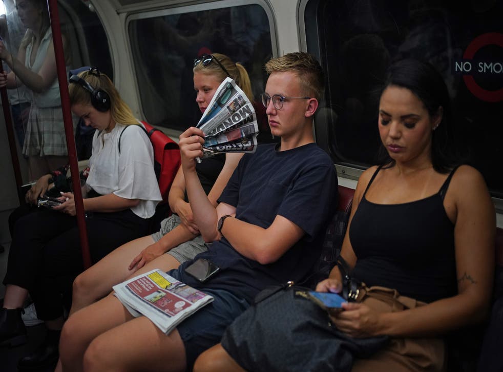 A passenger uses a newspaper as a fan while travelling on the Bakerloo line in central London (Yui Mok/PA)