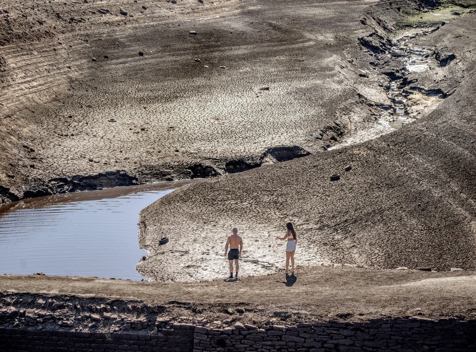 People walk on the dry cracked earth at Baitings Reservoir in Ripponden, 西约克, where water levels are significantly low (丹尼劳森/PA).