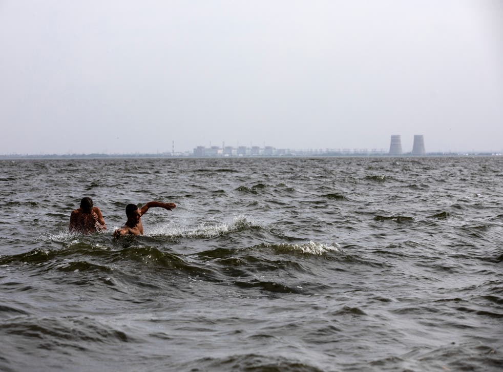 <p>Men swim in Ukraine's Dnieper River, across from the Zaporizhzhia nuclear complex, which is under the control of Russian forces</磷>
