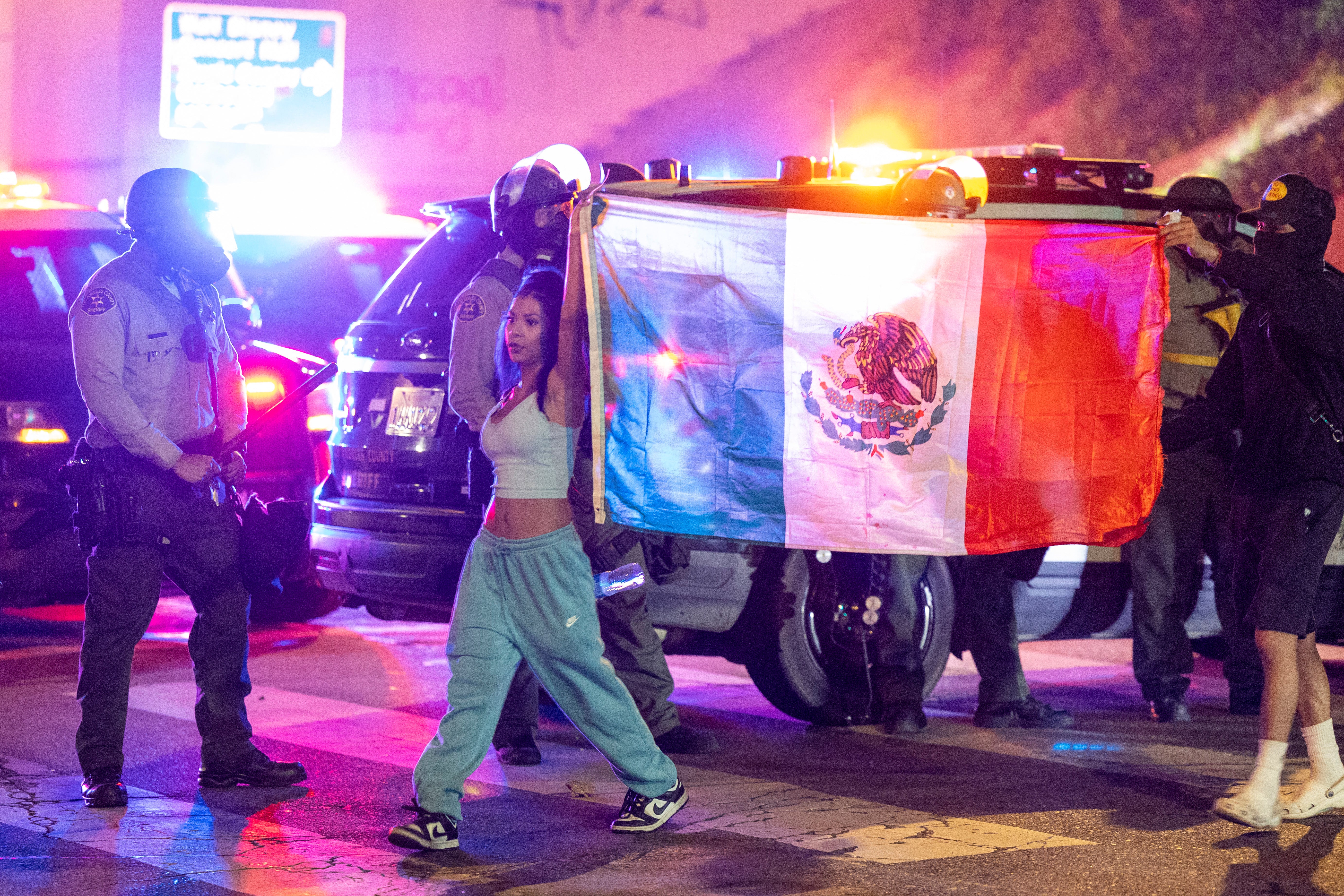 Protesters walk past Sheriff deputies with the Mexican flag on Sunday evening