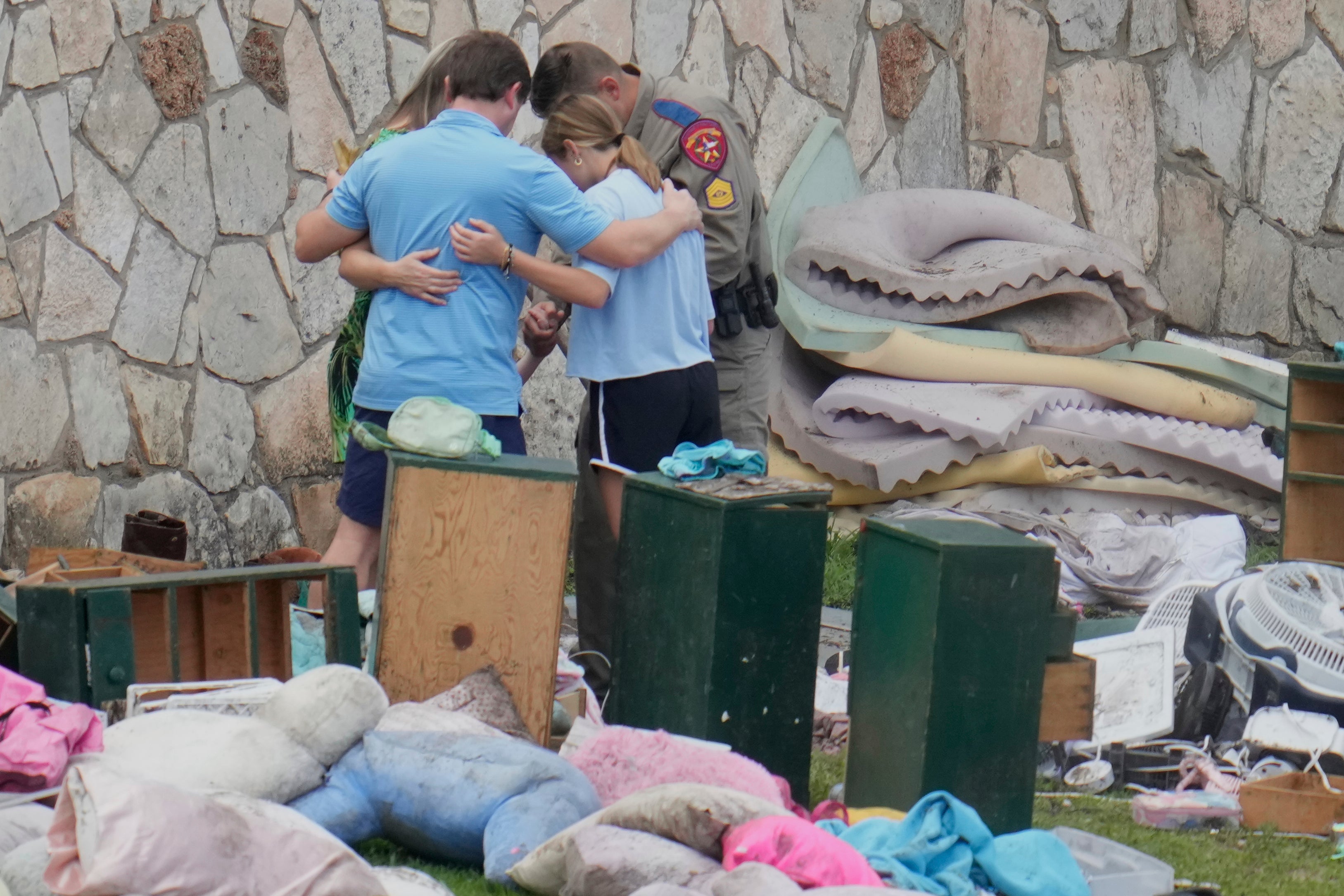 An officer prays with a family as they pick up items at Camp Mystic