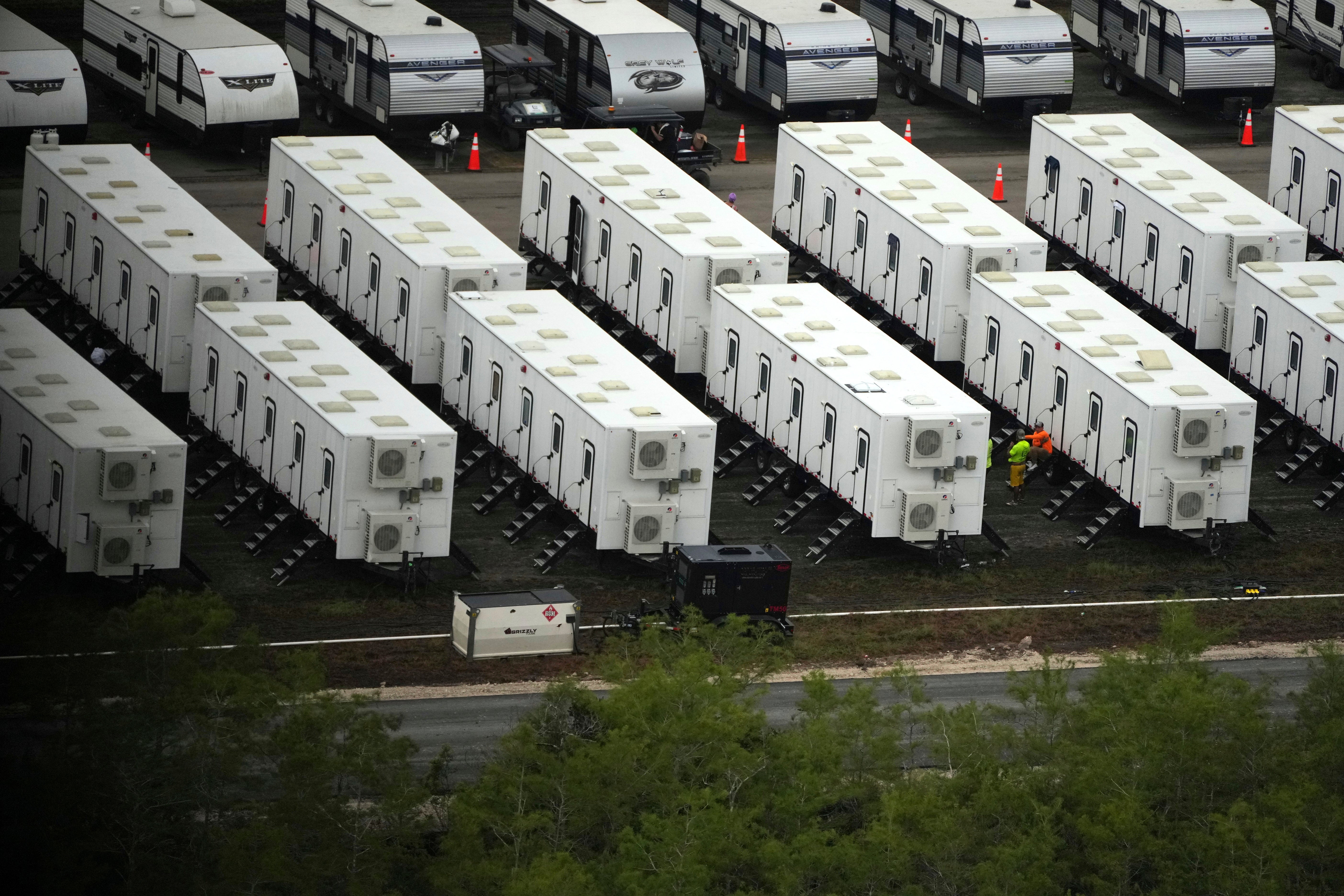 Workers sit alongside trailers as work progresses on a new migrant detention center dubbed