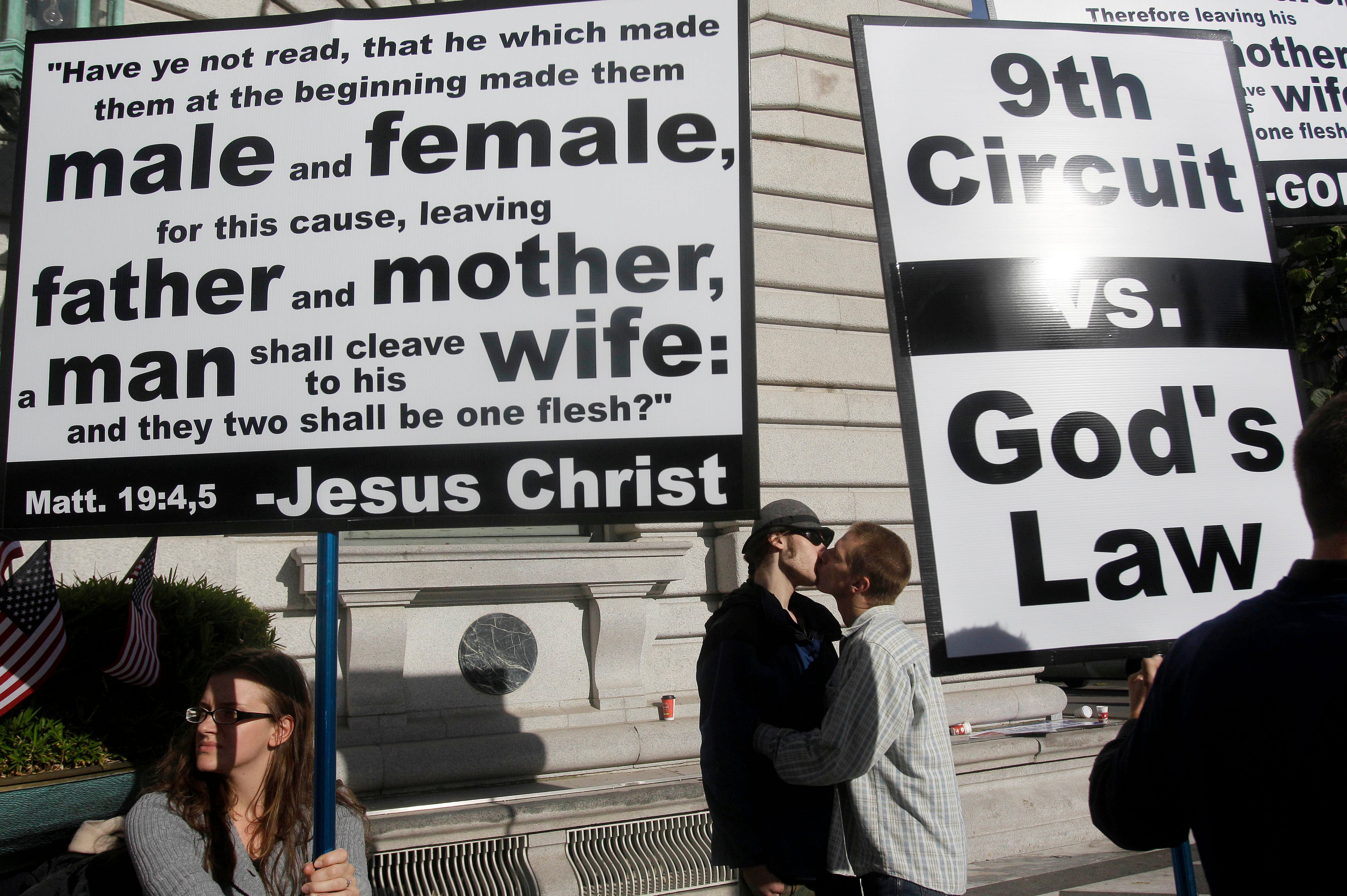 Aiden Lougee, center left, kisses his boyfriend, Rex Resa, seen between signs held by opponents to gay marriage outside of the courthouse after a hearing in the Ninth Circuit Court of Appeals, Monday, Dec. 6, 2010, in San Francisco. (AP Photo/Jeff Chiu, File)