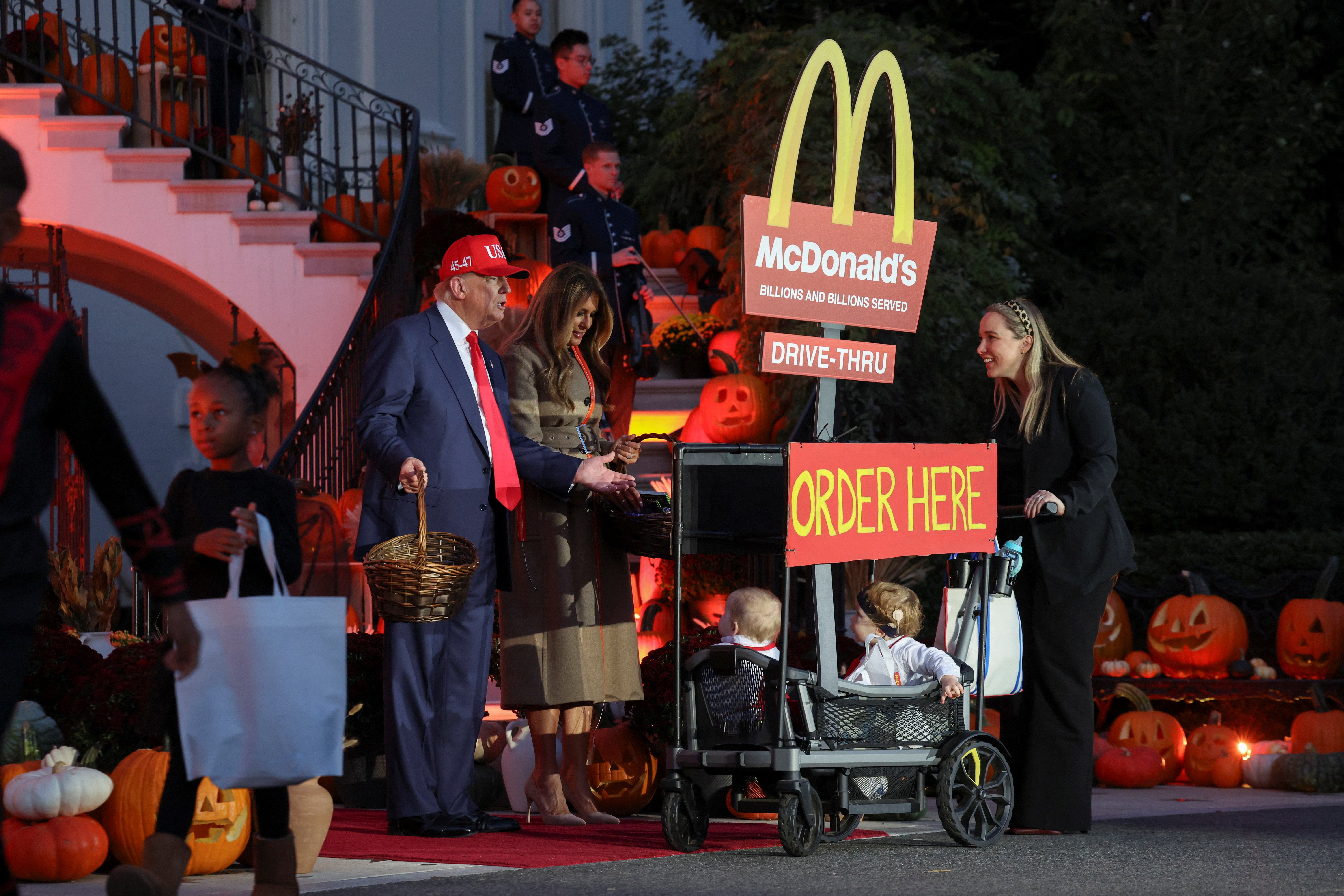 President Donald Trump and first lady Melania Trump greet two trick-or-treaters in a wagon with the McDonald's drive-thru sign at the White House Halloween event