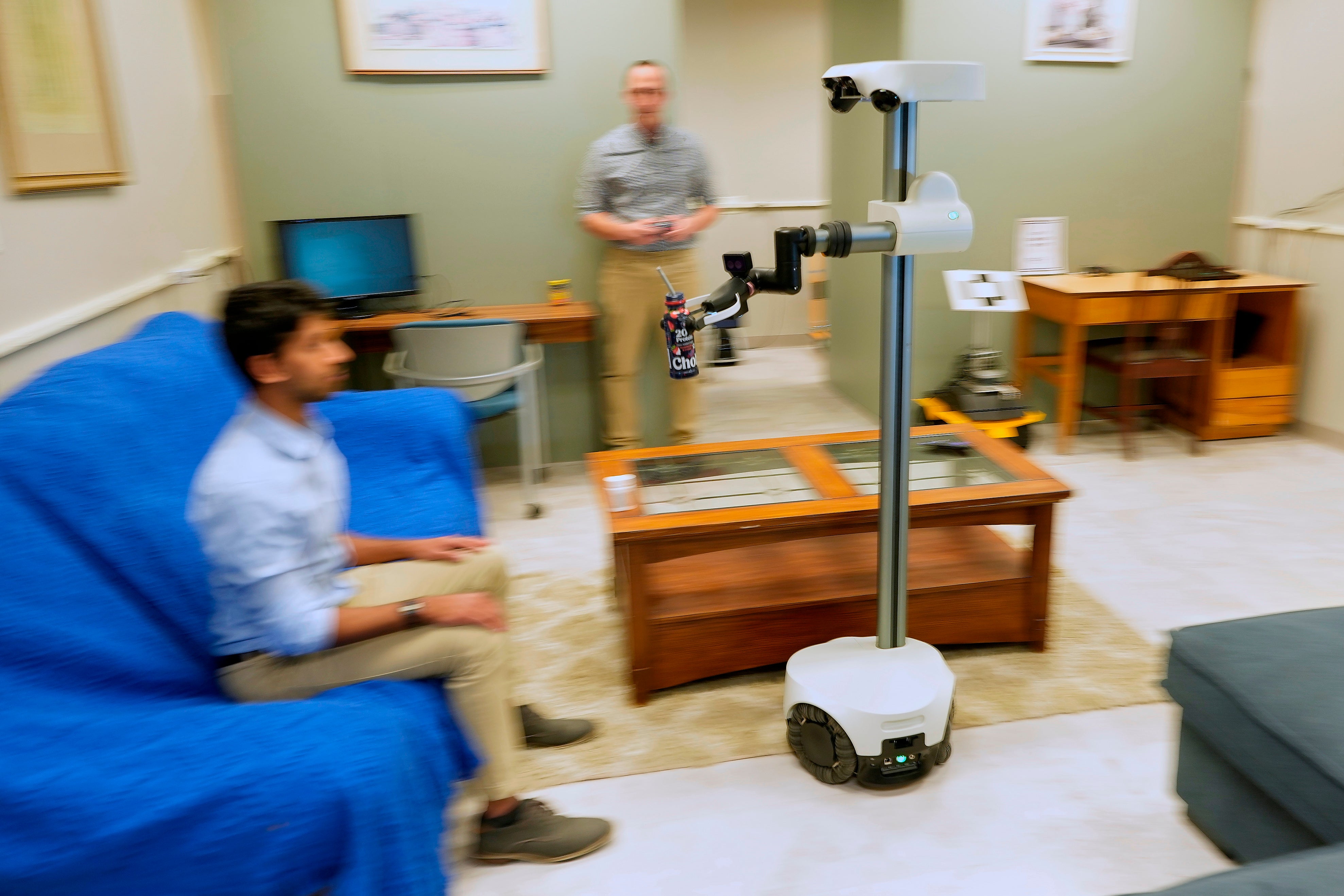A robot operated by a robotics engineer, rear, brings a drink to colleague during a demonstration at the University of New Hampshire