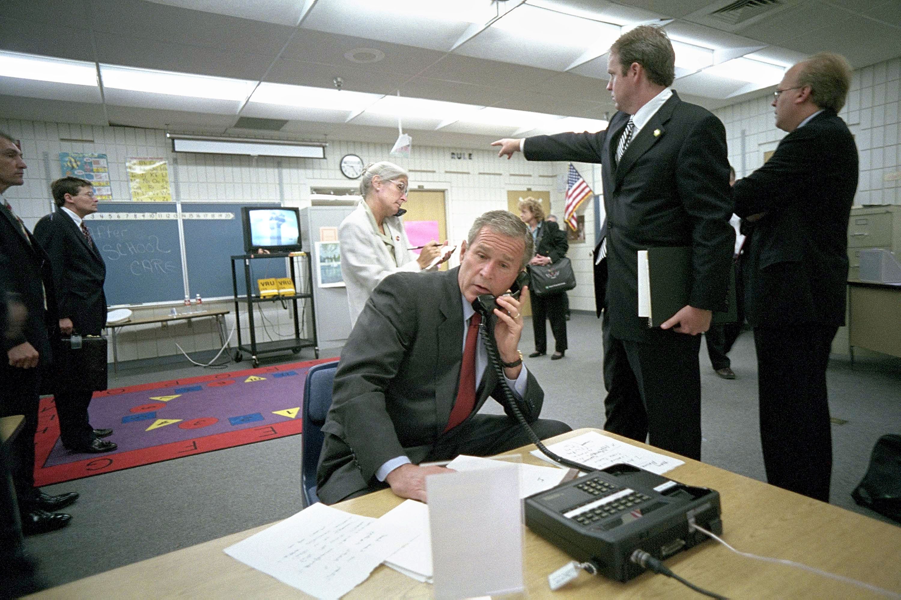 Bush makes a telephone call as White House Director Of Communications Dan Bartlett points to footage of the attack on the World Trade Center from Emma Booker Elementary School on Sept. 11, 2001