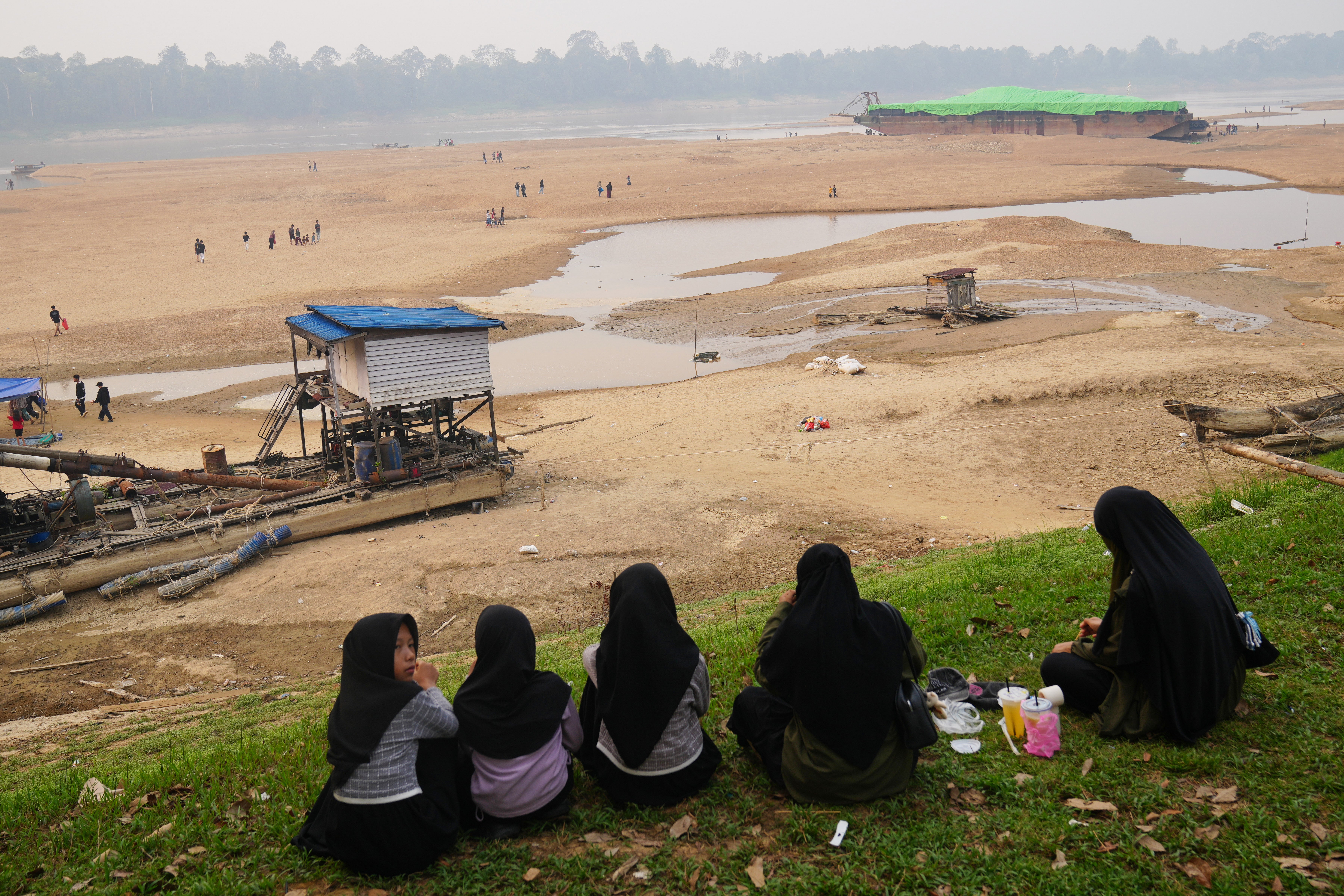 People look at a barge, back right, stranded on a dry riverbed of the Kapuas River amid a drought in Sekadau, West Kalimantan, Indonesia