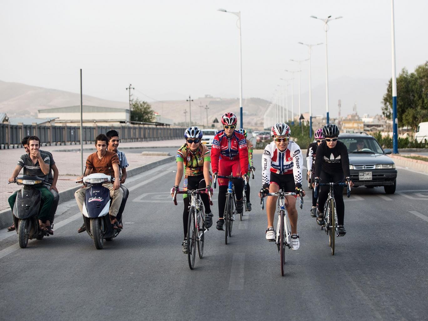 Newroz Sports Club cyclists pass young men on scooters during a training ride in Sulaimaniyah, Iraq