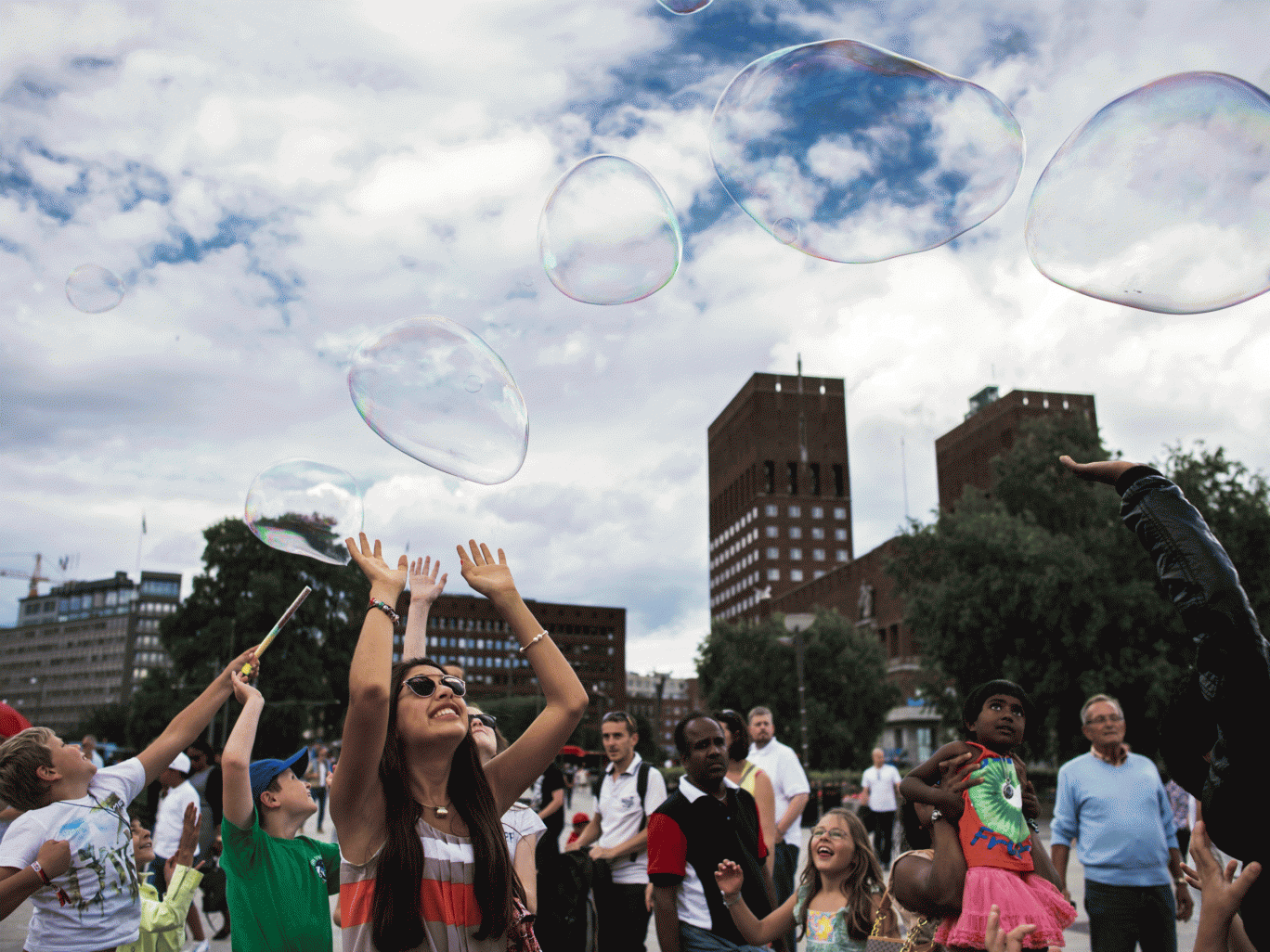 People try to catch soap bubbles created by a street artist by the waterfront next to the city hall in Oslo