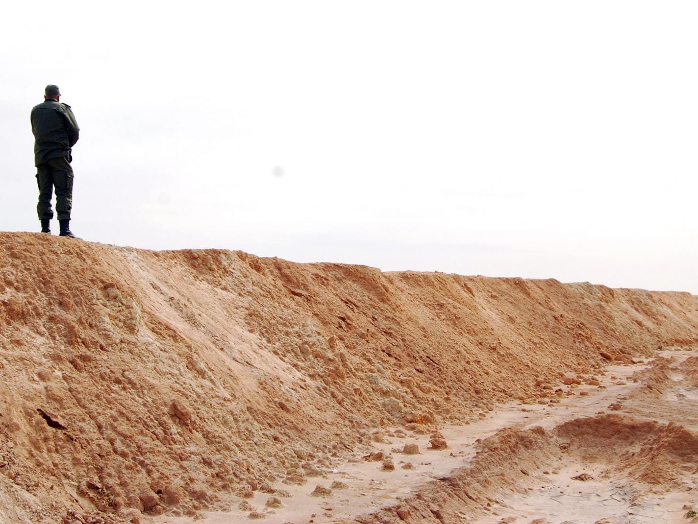 A solder stands on a fence erected by Tunisia on their border with Libya