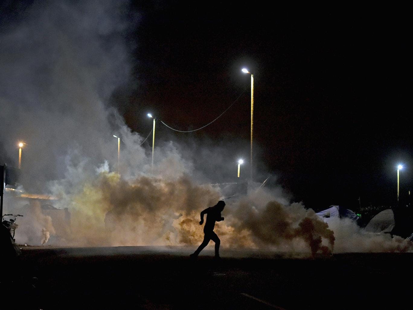 A refugee flees police tear gas near the entrance to the Jungle camp in Calais