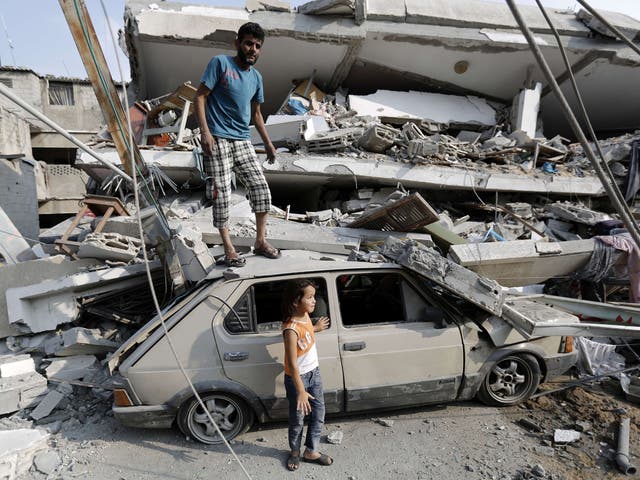 A Palestinian man stands on the wreckage of a car as he searches the rubble of his destroyed apartment for belongings following an Israeli air strike in the center of Gaza City  