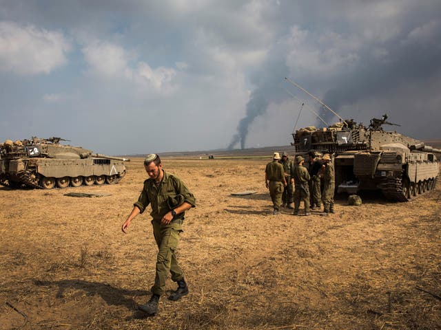 Israeli soldiers stand near their tank while smoke due to airstrikes and shelling rises from Gaza near Sderot 