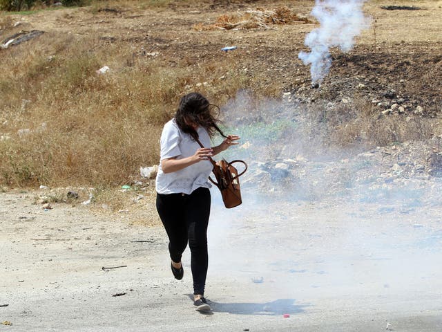A Palestinian woman runs to seek cover from tear gas  fired by Israeli soldiers during  clashes at a protest against the Israeli attacks on Gaza Strip, at Howwara checkpoint near the west bank city of Nablus  