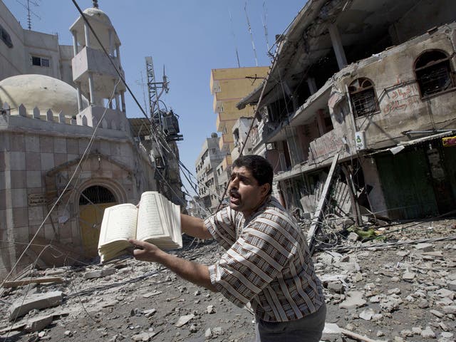 A Palestinian man holds a copy of the Koran, Islam's holy book, near a heavily damaged mosque following an Israeli military strike in Gaza city 