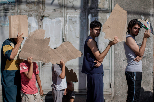 Palestinians used pieces of cardboard as protection from the sun while queuing up in front of a bakery in Gaza City. A seven-hour humanitarian ceasefire called by Israel went into effect in most of the Gaza Strip, after an attack that killed 10 people at a UN-run school