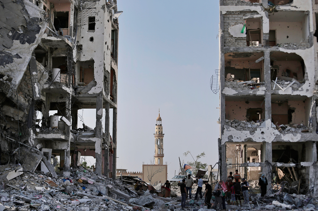 Backdropped by the damaged minaret of the Al-Azba mosque, Palestinians inspect the damage to the Nada Towers residential neighborhood in the town of Beit Lahiya, northern Gaza Strip