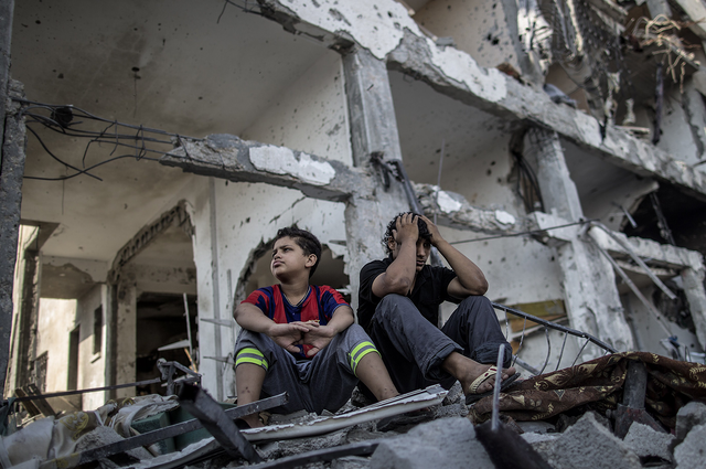 Palestinian brothers sit on the rubble of their house in front of an apartment block in part of the northern Beit Hanun district of the Gaza Strip after a 72-hour truce accepted by Israel and Hamas came into effect