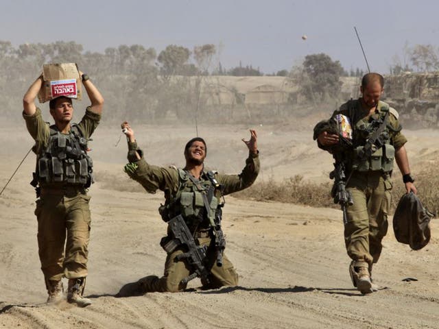 An Israeli soldier gestures in relief as he walks with comrades near the border between Israel and the Gaza Strip after returning from the Hamas-controlled Palestinian coastal enclave