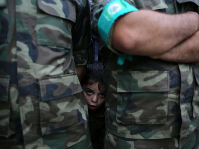 A Palestinian boy peaks from behind Palestinian militants of the Ezzedine al-Qassam brigade, the armed wing of Hamas, during a rally to commemorate the 27th anniversary of the Islamist movement's creation