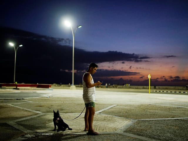Doctor Alejandro Soto stands with his dog Coco as he connects to an internet hotspot in Havana