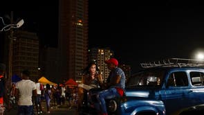 A woman sits on a vintage car as she uses a hotspot in Havana