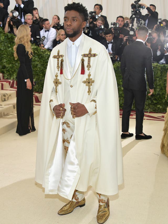 Black Panther's Chadwick Bosemanan wears an all-white Versace outfit with religiously inspired embellishments, gold shoes, and a cape