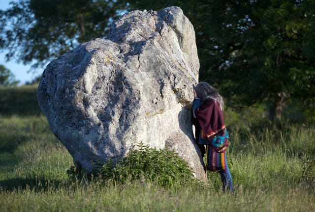A person touches one of the stones at the Avebury stone circle in Wiltshire, where people gathered to celebrate the Summer Solstice on June 21