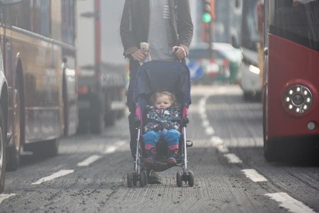 A child is wheeled between buses on a busy road in London