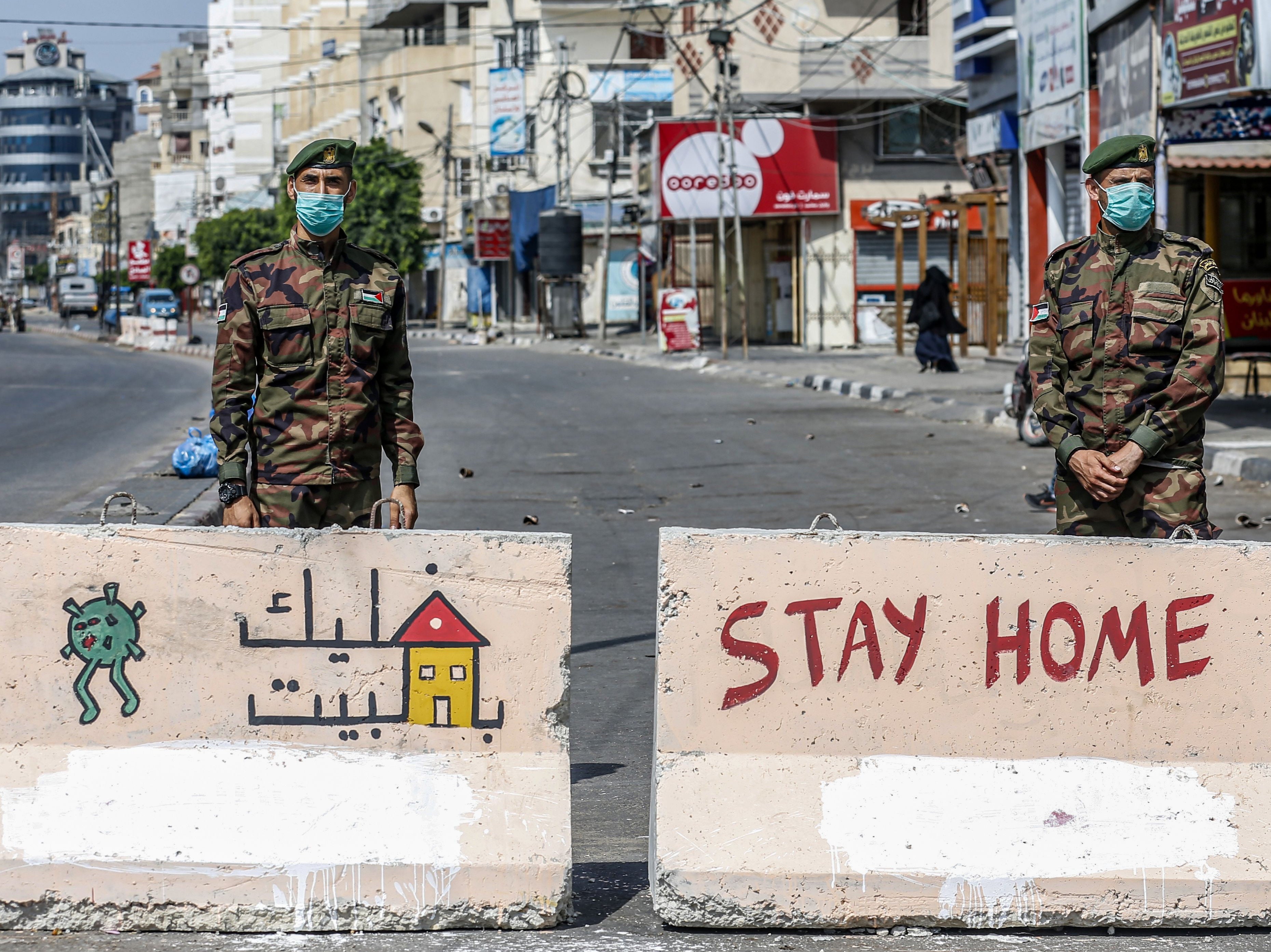 Mask-clad policemen loyal to Hamas stand behind concrete barriers painted with messages instructing people to remain at home at a checkpoint in Rafah in the southern Gaza Strip