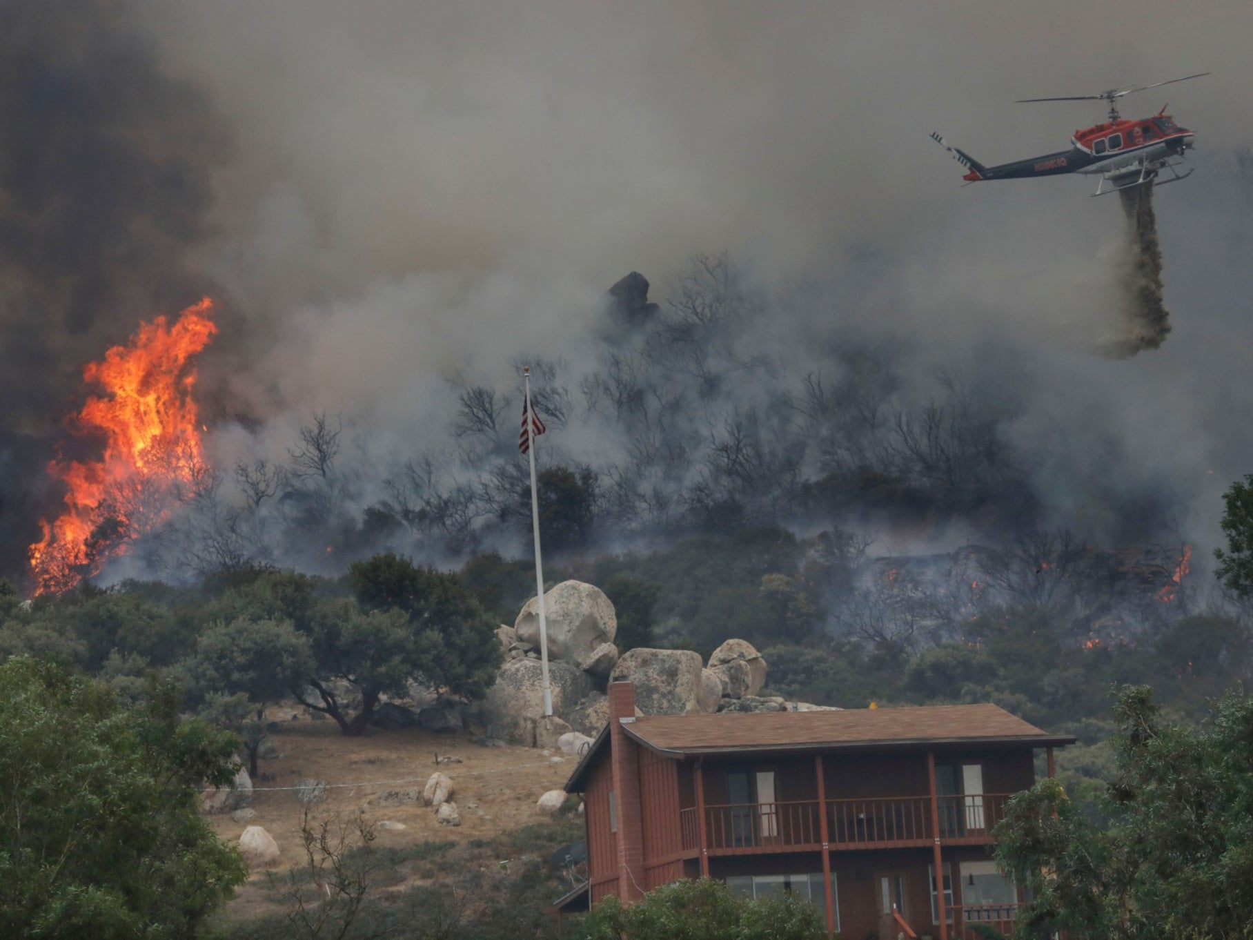 A brush fire encroaches along Japatul Road as a helicopter drops water during the Valley Fire in Jamul, California