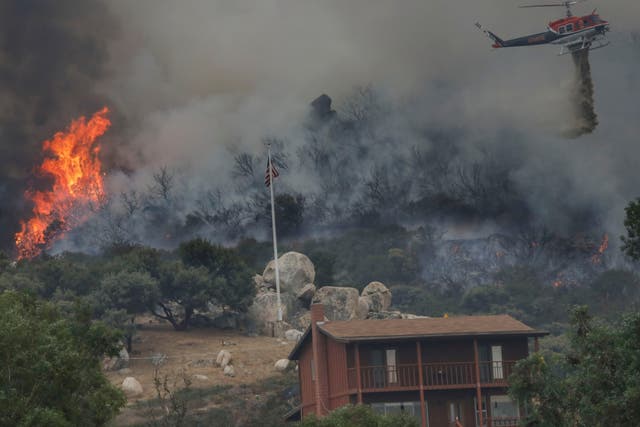 A brush fire encroaches along Japatul Road as a helicopter drops water during the Valley Fire in Jamul, California
