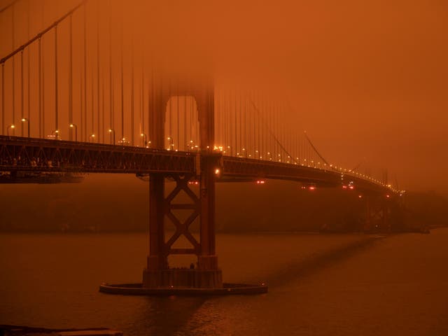 Cars drive along the San Francisco Bay Bridge under an orange smoke filled sky as more than 300,000 burn across California, including 35 major wildfires
